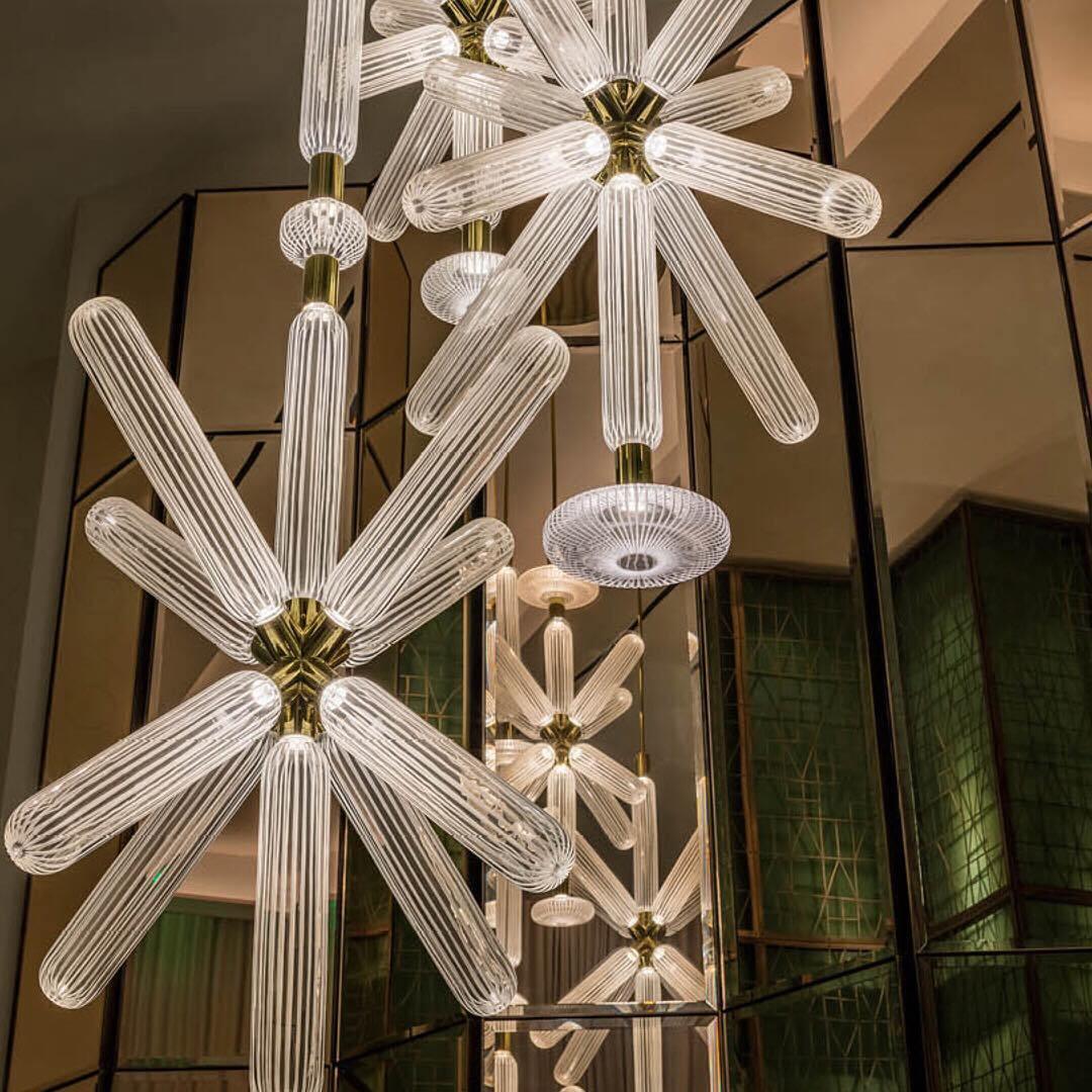 Clustered Clérachic pendants glow beside green glass panels, seen from below in a lobby.
