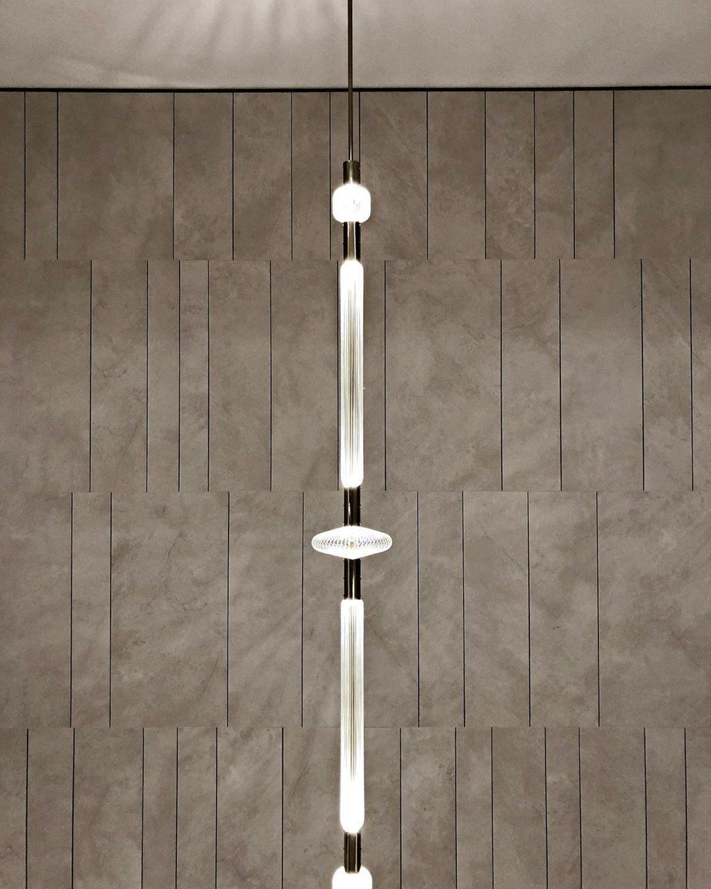 This Clérachic pendant hangs against a stone-tiled wall, its slim rod broken by a round disc joint.