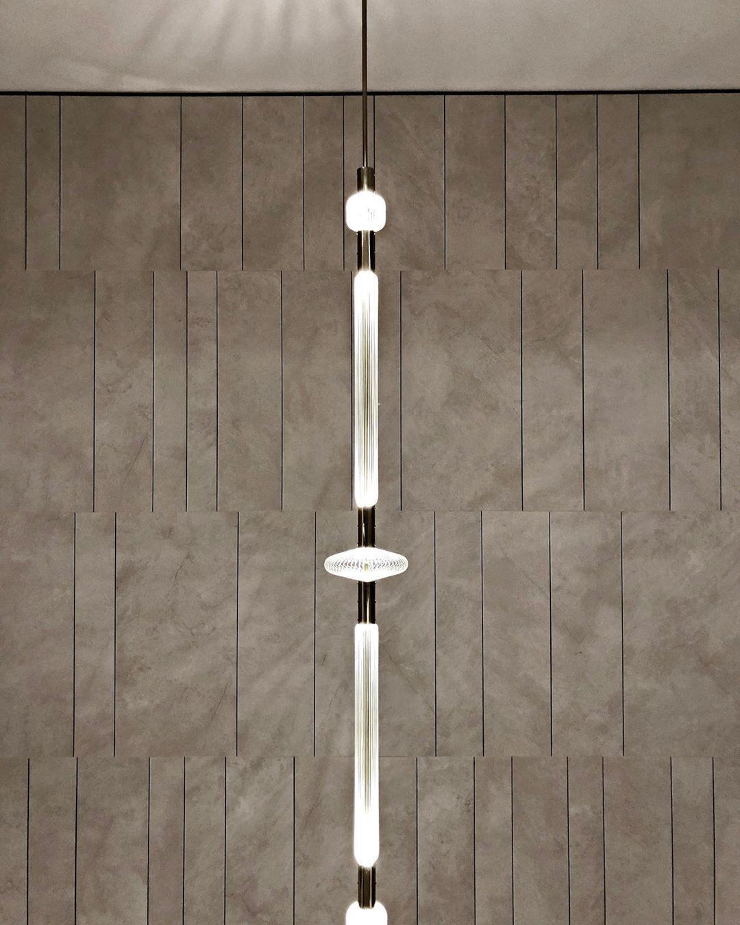 This Clérachic pendant hangs against a stone-tiled wall, its slim rod broken by a round disc joint.