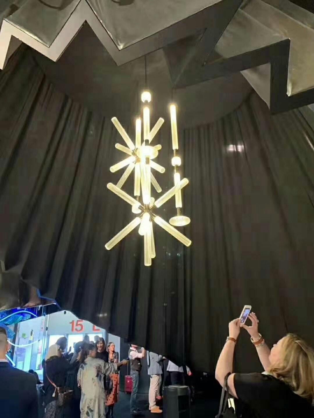 This Clérachic pendant hangs lit at a trade-show display, its crystal rods glowing above onlookers.