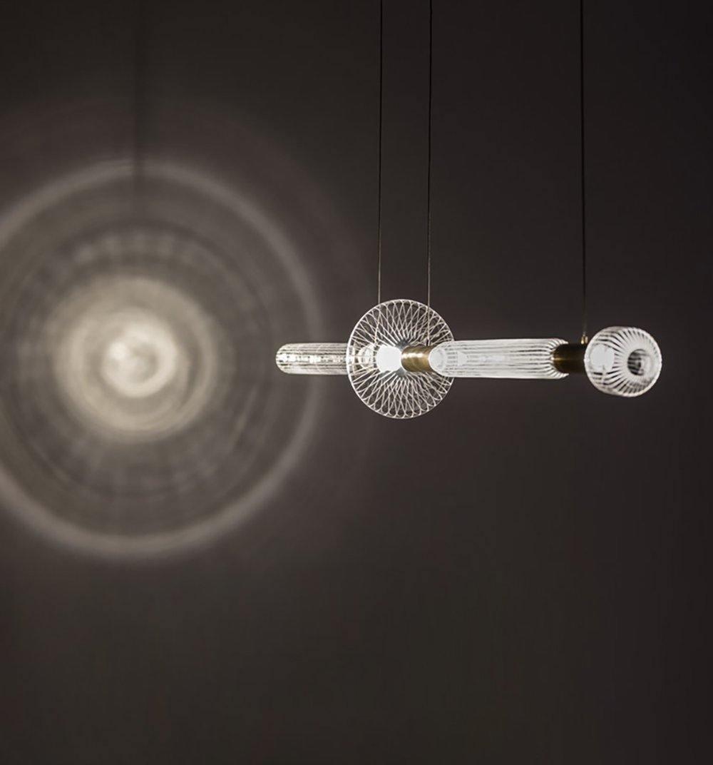 This Clérachic pendant glows against a dark wall, its light spreading in soft rings behind it.