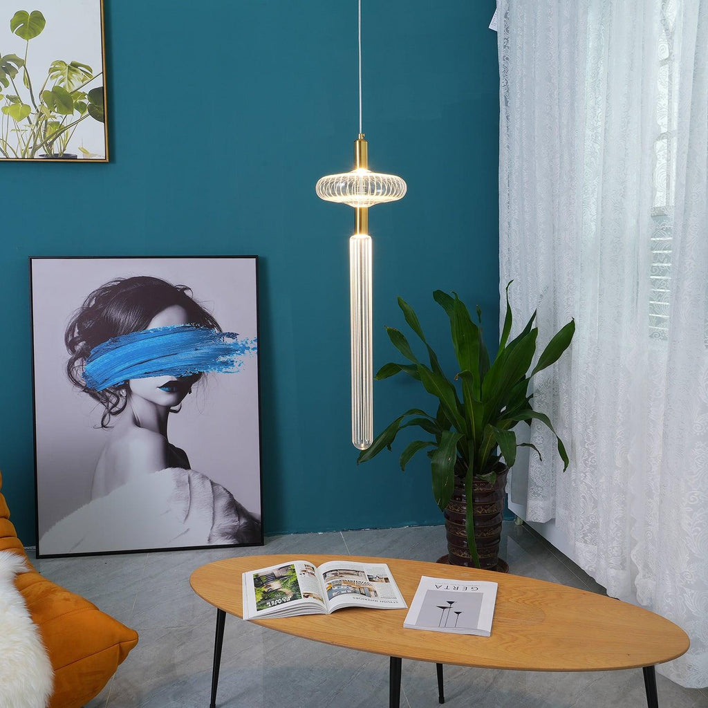 A single Clérachic pendant on a slim rod hangs lit beside a potted plant against a teal wall.