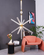 A large Clérachic pendant glows in a grey room, its crystal rods lit beside a coral chair and potted plant.