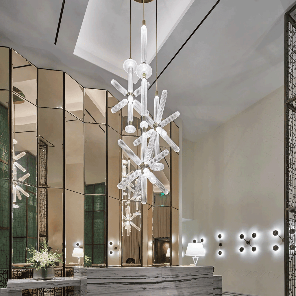 A tall Clérachic pendant with cascading crystal rods is reflected in the mirrored panels of a lobby.