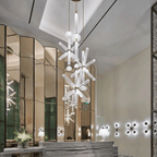 A tall Clérachic pendant with cascading crystal rods is reflected in the mirrored panels of a lobby.