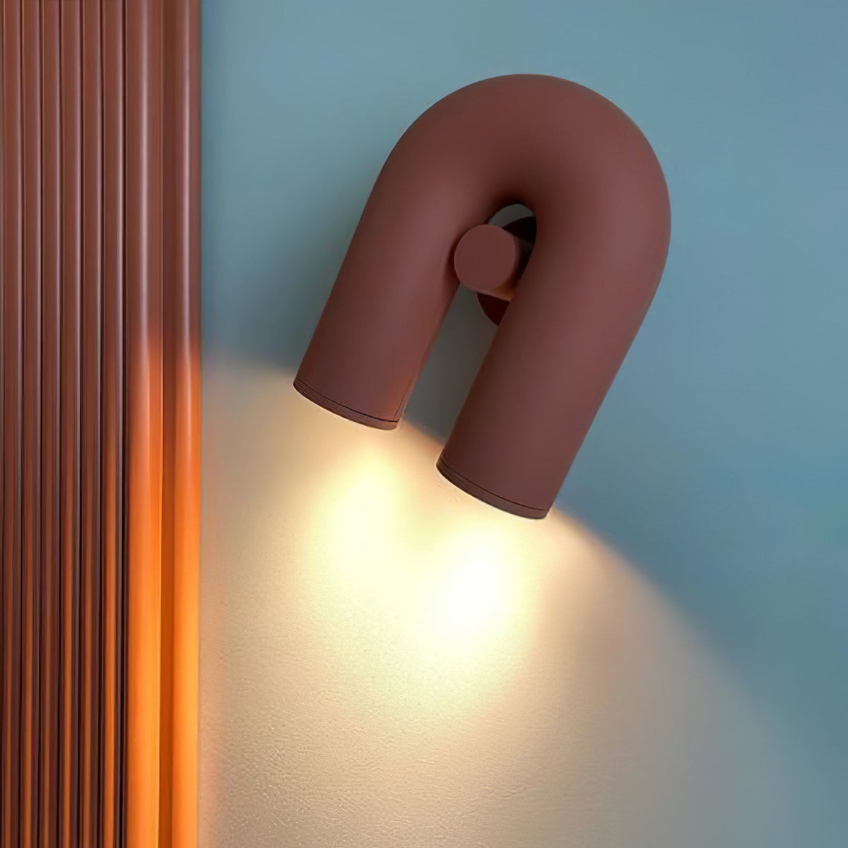 Angled beside a fluted wood panel, this terracotta Clérachic wall light glows warm against a blue wall.