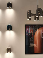 Grey, teal and terracotta Clérachic wall lights stack on a wall beside a multi-head floor lamp and framed poster.