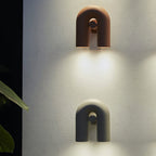 Two Clérachic wall lights, terracotta above black, light a textured plaster wall with warm downward glow.