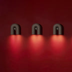 Three black Clérachic wall lights line a deep red wall, each glowing with a warm reddish light below.