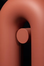Close-up of the curved top and round swivel knob on this terracotta Clérachic wall light, against black.