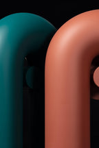 Close-up of two Clérachic wall lights, teal and terracotta, with their curved tops side by side against black.