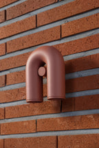 A terracotta Clérachic wall light mounts on an exposed red-brick wall, unlit, its swivel heads pointing down.