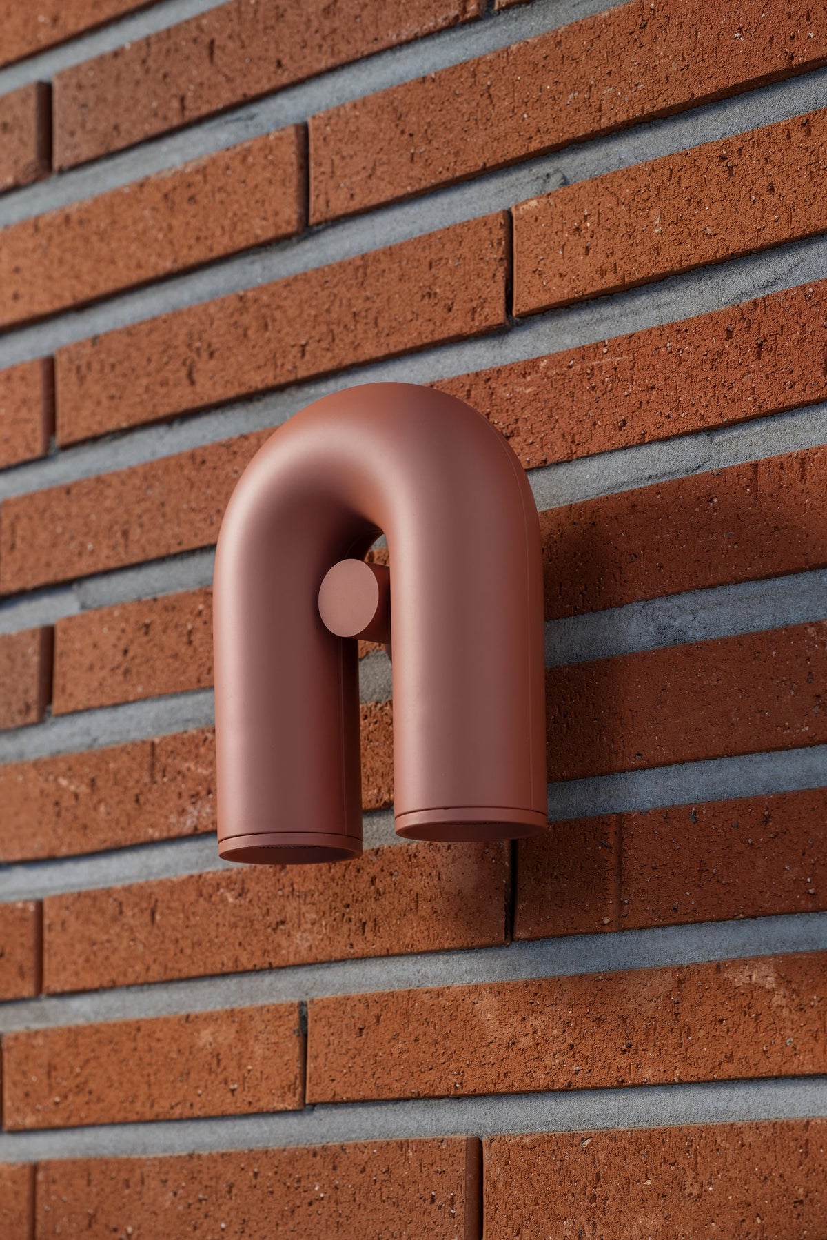 A terracotta Clérachic wall light mounts on an exposed red-brick wall, unlit, its swivel heads pointing down.