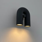 This Clérachic wall light in black casts a warm pool of downlight onto the grey wall below its U-shaped tube.