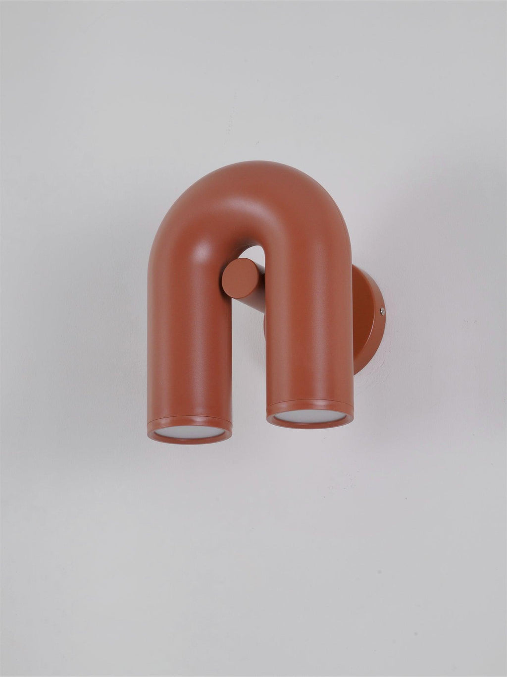 This terracotta Clérachic wall light angles to show its mounting plate against a plain grey backdrop.