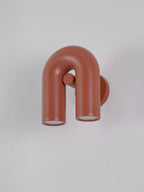 This terracotta Clérachic wall light angles to show its mounting plate against a plain grey backdrop.
