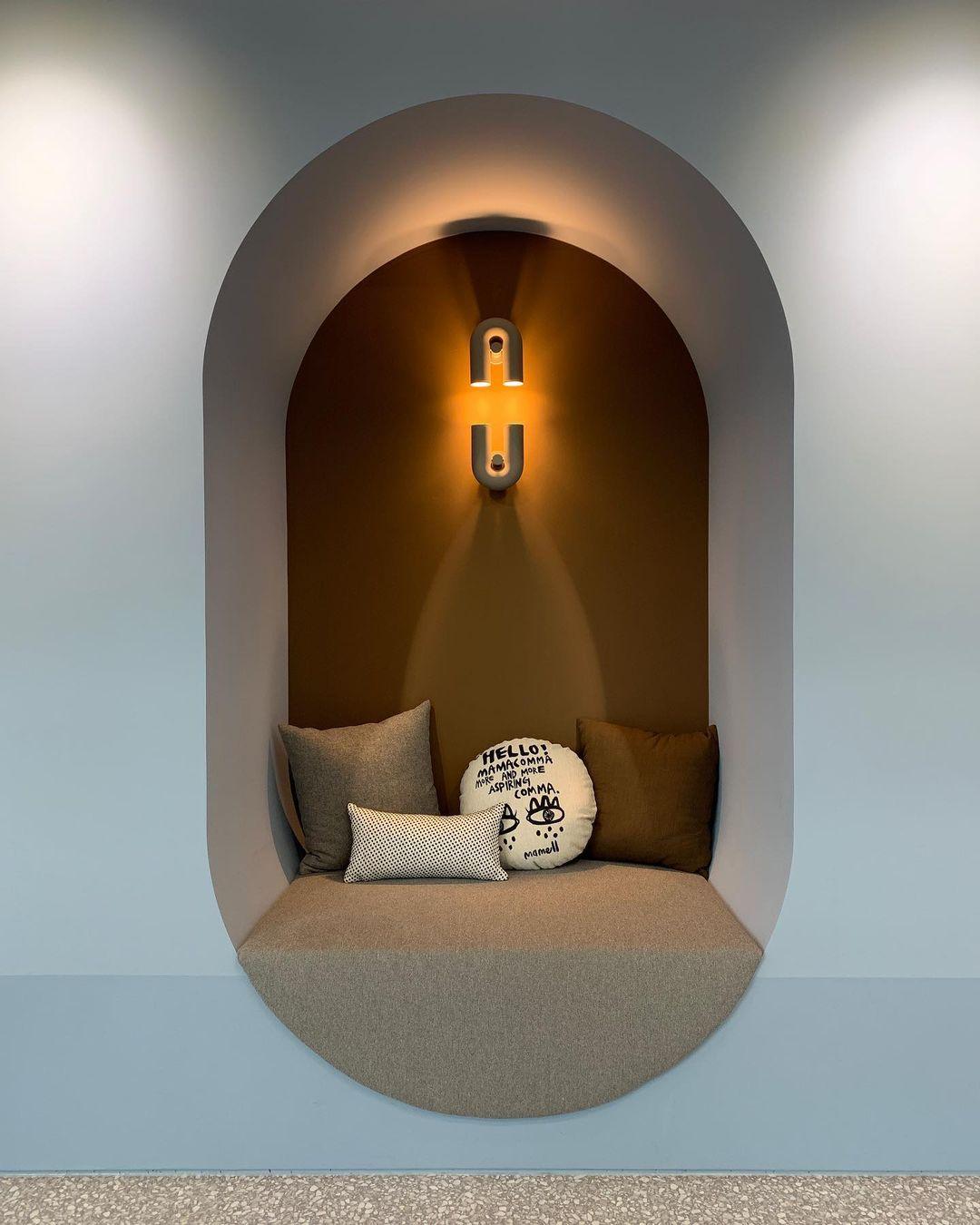 In a mustard-toned alcove with a cushioned bench seat, this terracotta Clérachic wall light glows warm overhead.