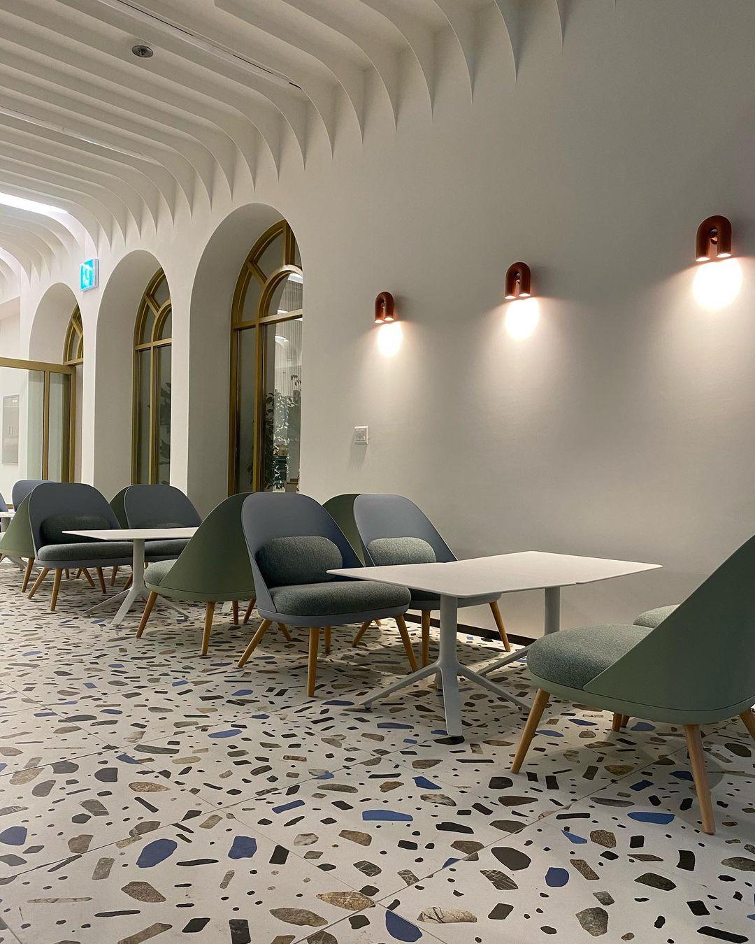 Terracotta and black Clérachic wall lights glow along an arched corridor above a terrazzo-floored lounge area.