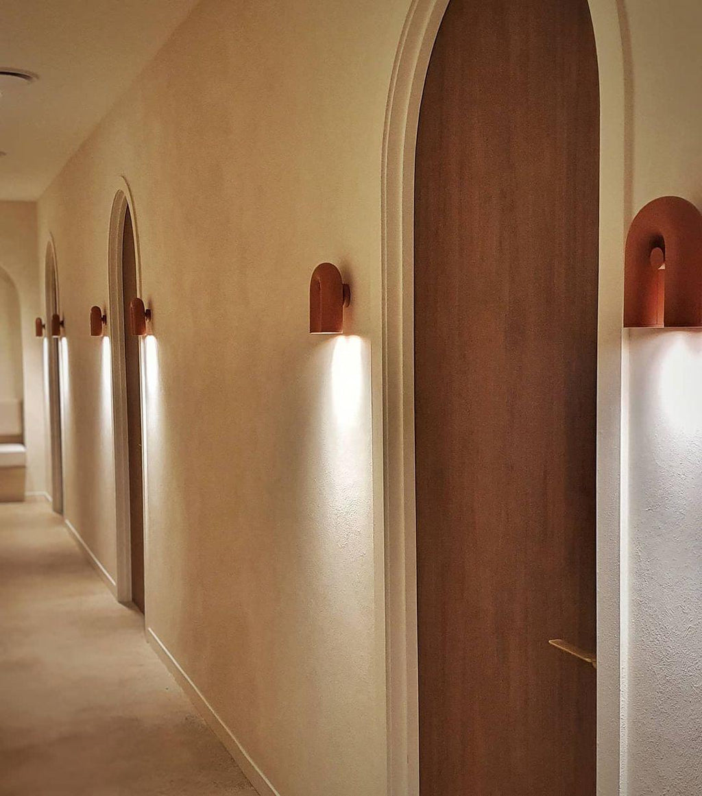 Terracotta Clérachic wall lights line an arched hallway with wooden doors, each glowing warm along the corridor.