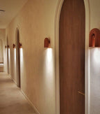 Terracotta Clérachic wall lights line an arched hallway with wooden doors, each glowing warm along the corridor.
