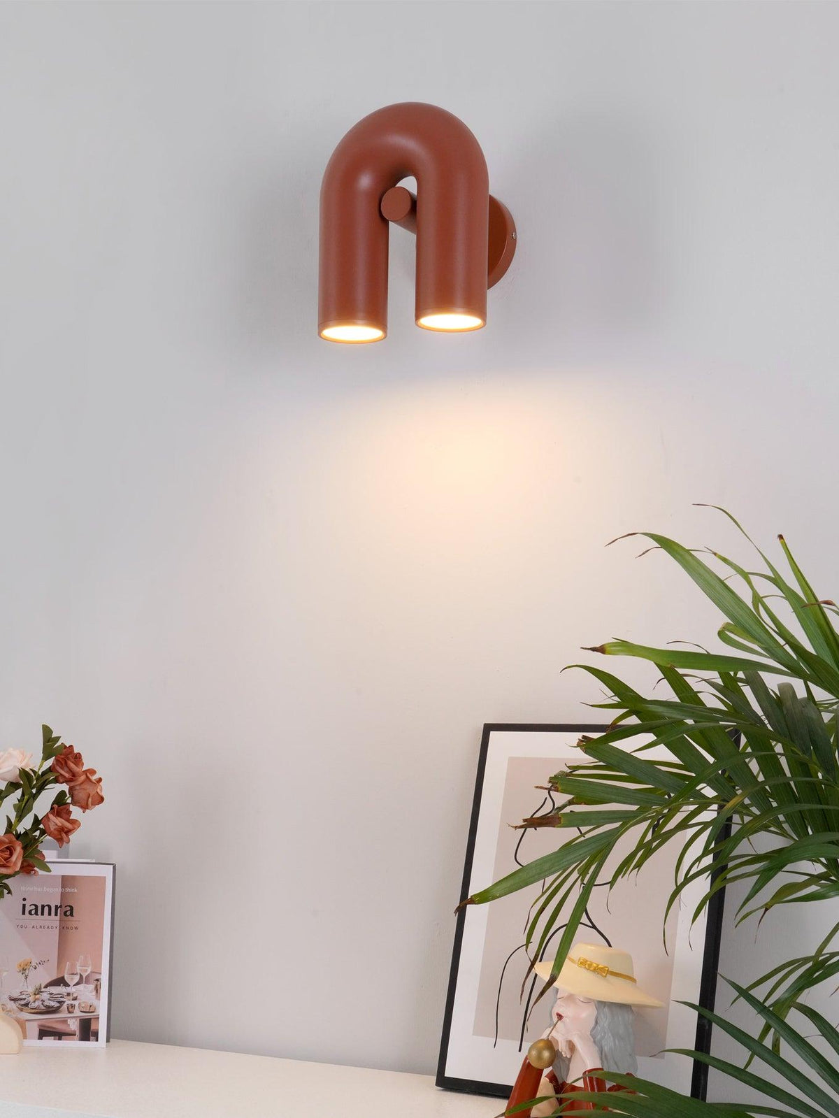 Mounted above a plant-topped console table, this terracotta Clérachic wall light glows warm in a home setting.
