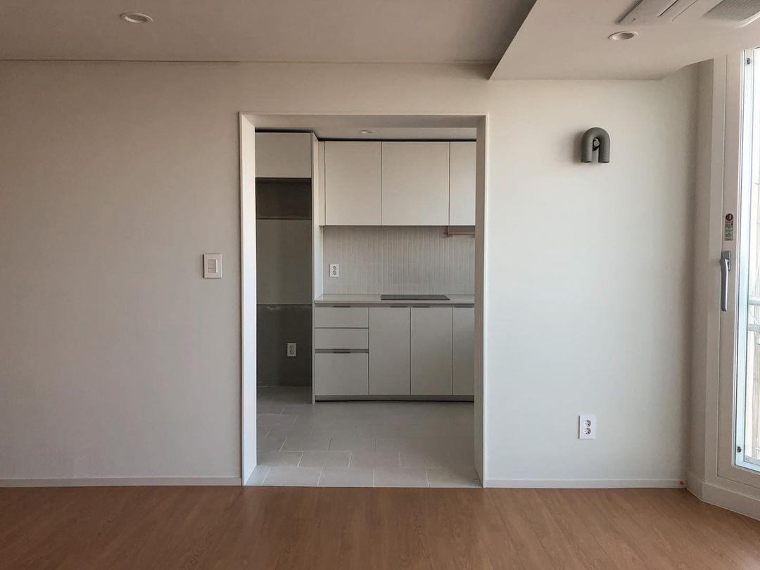 Small and unlit, this Clérachic wall light sits on a far wall of an empty apartment room near the kitchen doorway.