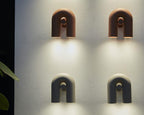Four Clérachic wall lights, terracotta above and black below, glow in a 2x2 arrangement on a textured wall.