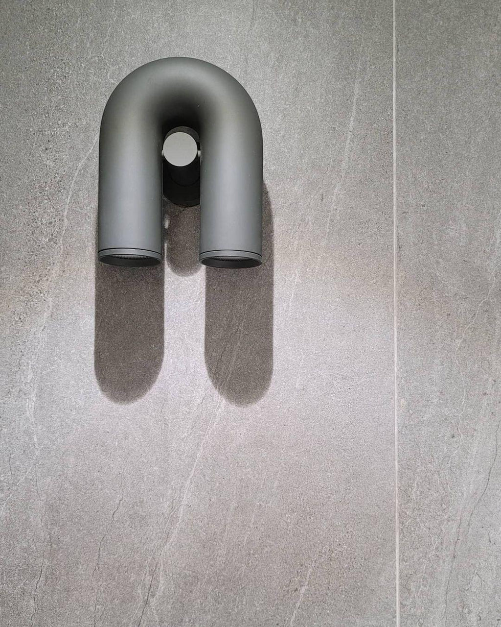 Mounted at an angle on a textured stone wall, this grey Clérachic wall light sits unlit.