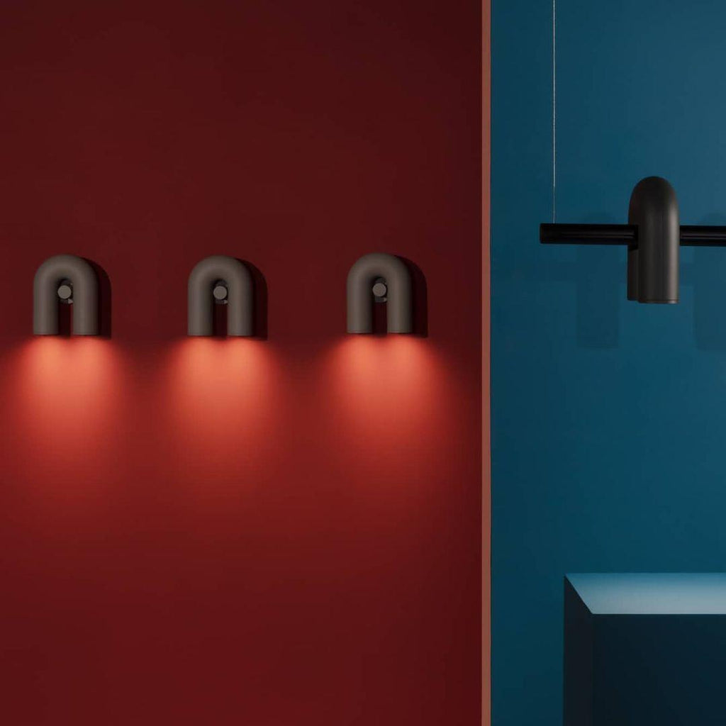 Three Clérachic wall lights in black cast warm downlight along a red wall, seen from below.