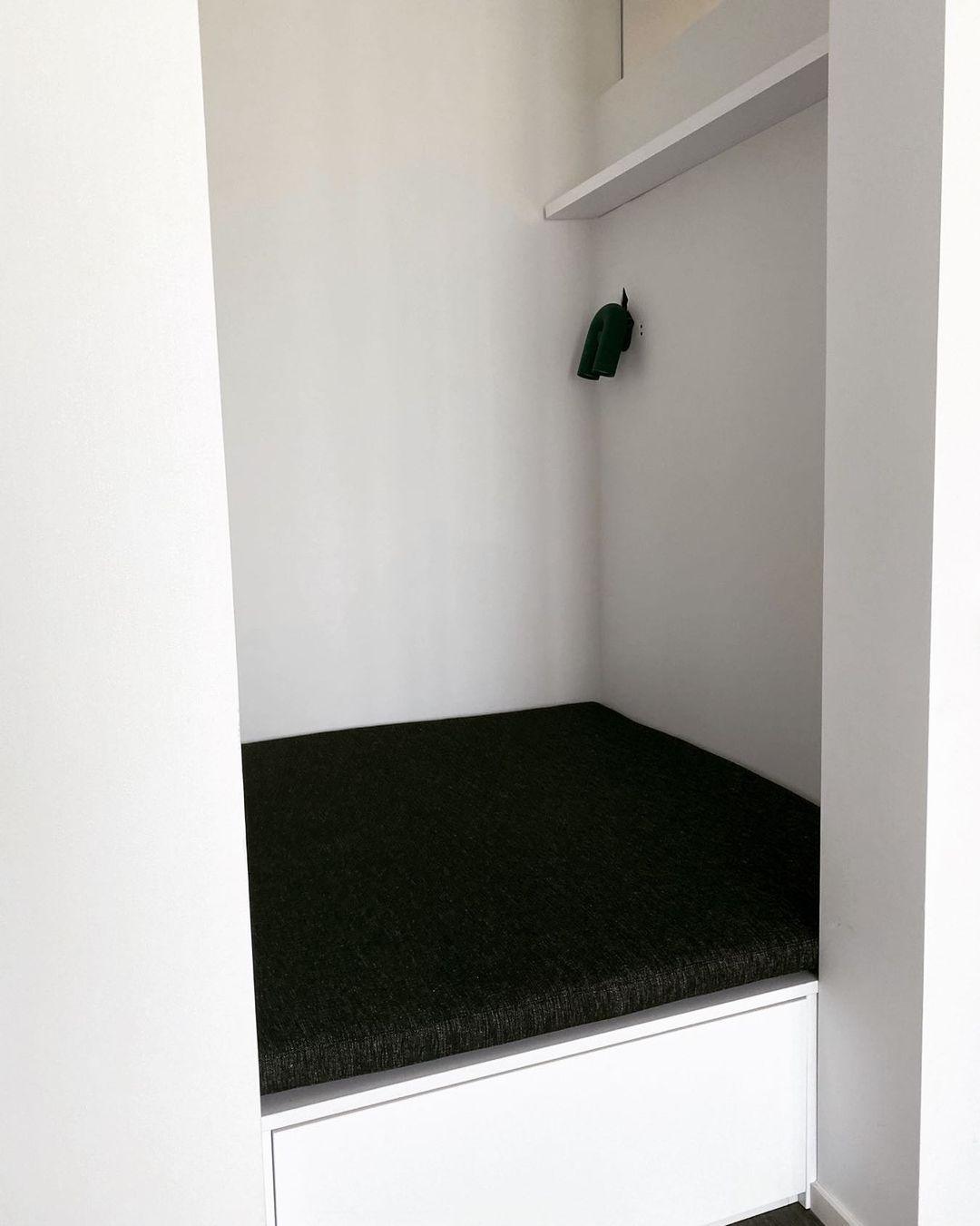 This Clérachic wall light in black mounts small and unlit above a built-in bench with a dark cushioned seat.
