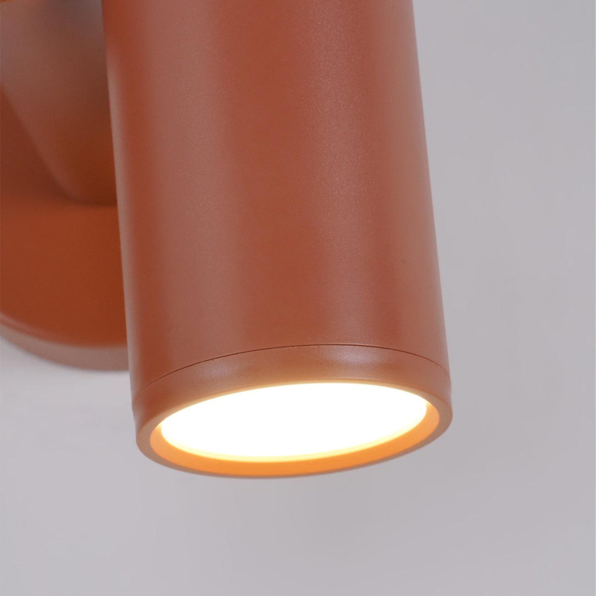 Close-up of one spotlight head on this terracotta Clérachic wall light, glowing warm against a grey background.