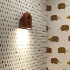 This terracotta Clérachic wall light lights a hedgehog-print wallpaper beside a matching patterned wall.