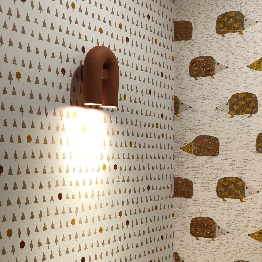 This terracotta Clérachic wall light lights a hedgehog-print wallpaper beside a matching patterned wall.