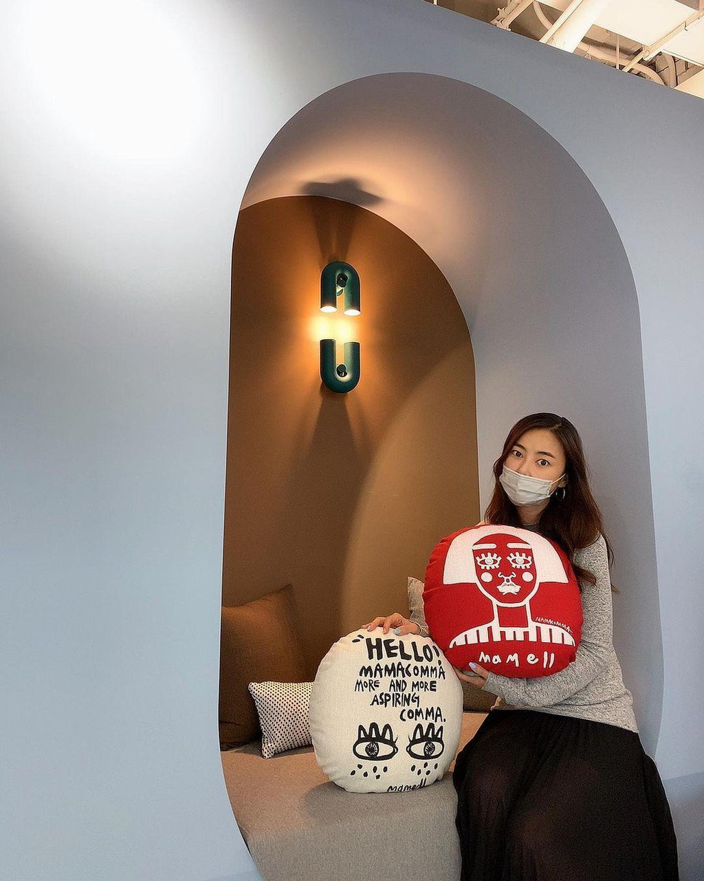 In an arched nook, this teal Clérachic wall light glows warm above a woman seated on a cushioned bench.