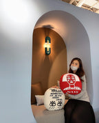 In an arched nook, this teal Clérachic wall light glows warm above a woman seated on a cushioned bench.