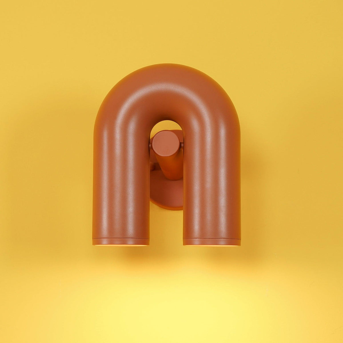 On a bold yellow backdrop, this terracotta Clérachic wall light pools warm light below its twin spotlight heads.