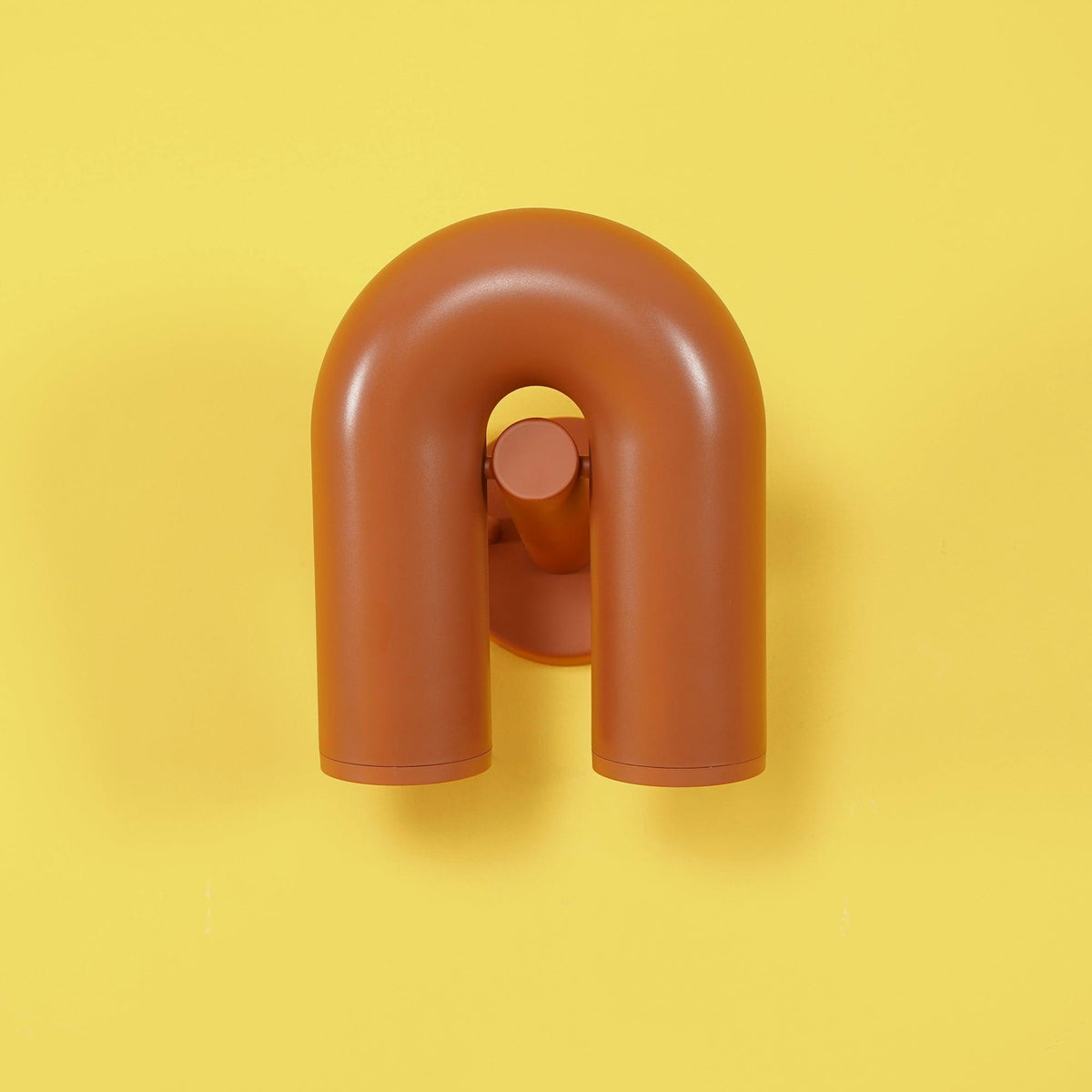 This terracotta Clérachic wall light stands unlit on a bright yellow backdrop, angled slightly forward.