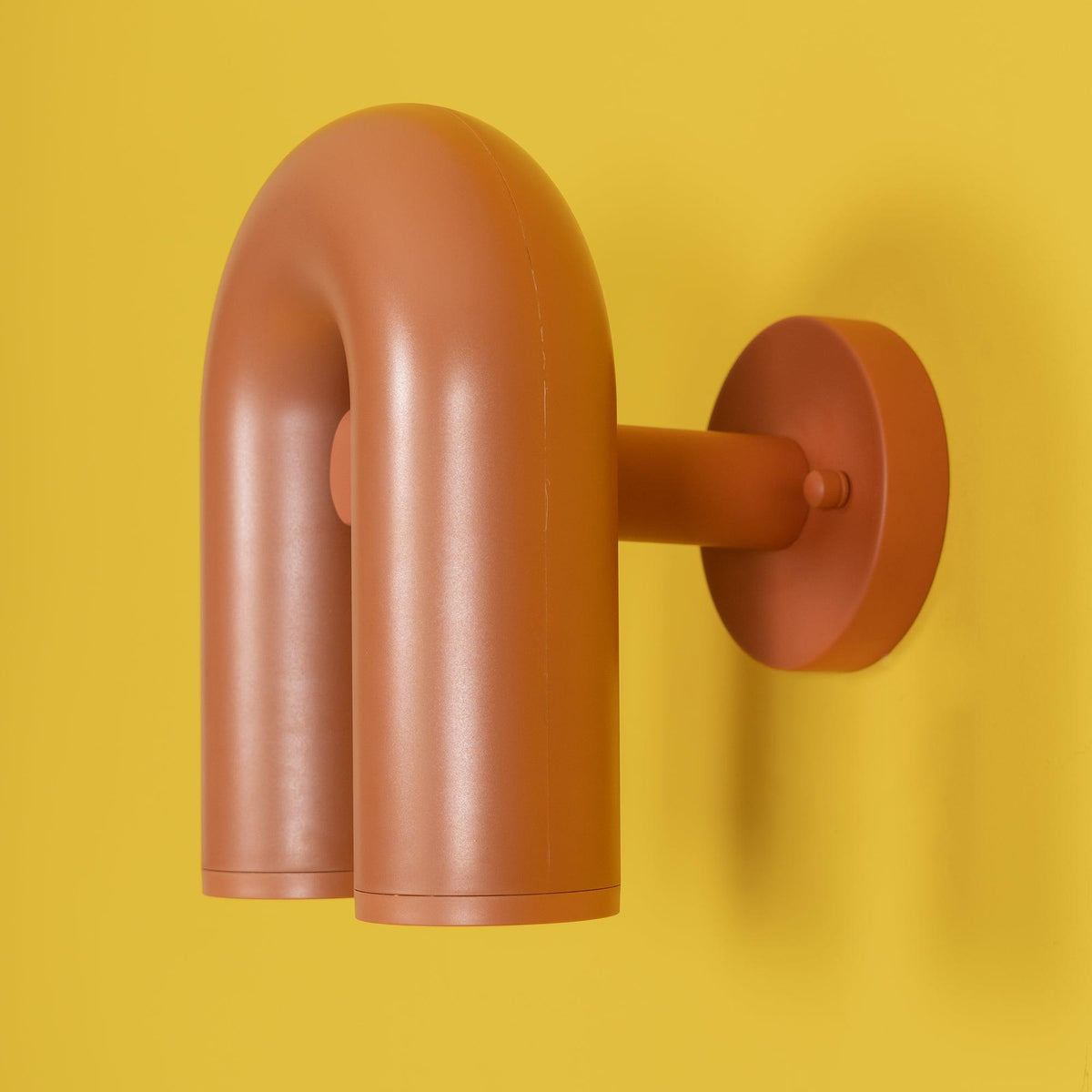 Full side profile of this terracotta Clérachic wall light shows its mounting arm against a yellow backdrop, unlit.