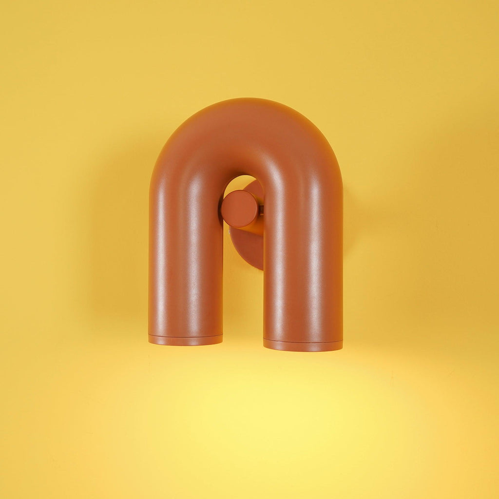 Centred on a yellow backdrop, this terracotta Clérachic wall light glows warm from its twin spotlight heads.