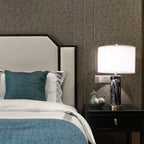 The Clérachic table lamp lights a nightstand between a teal cushion and a grey throw at the foot of the bed.