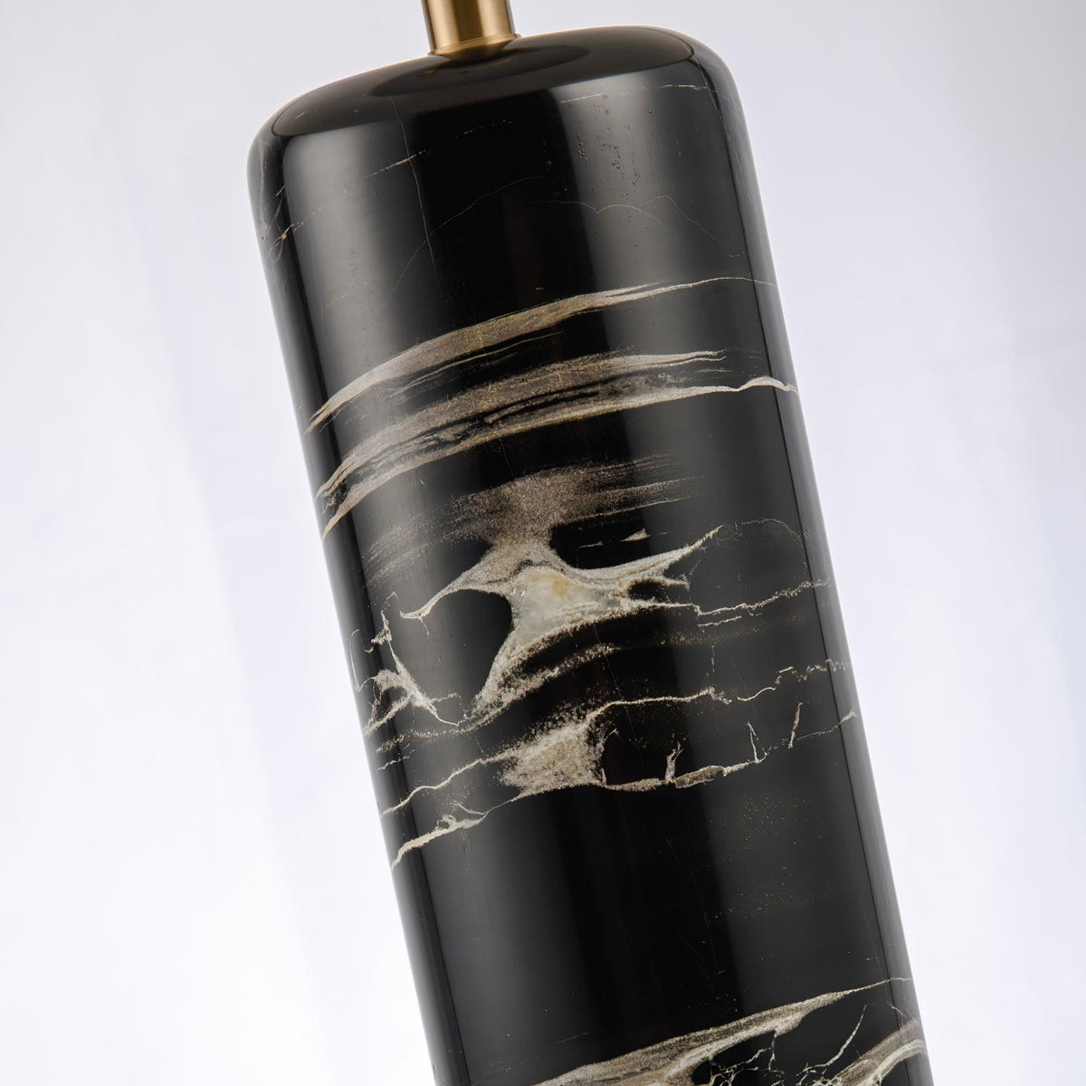 A diagonal close-up of the Clérachic table lamp's marble column and brass cap, cropped tight on the texture.