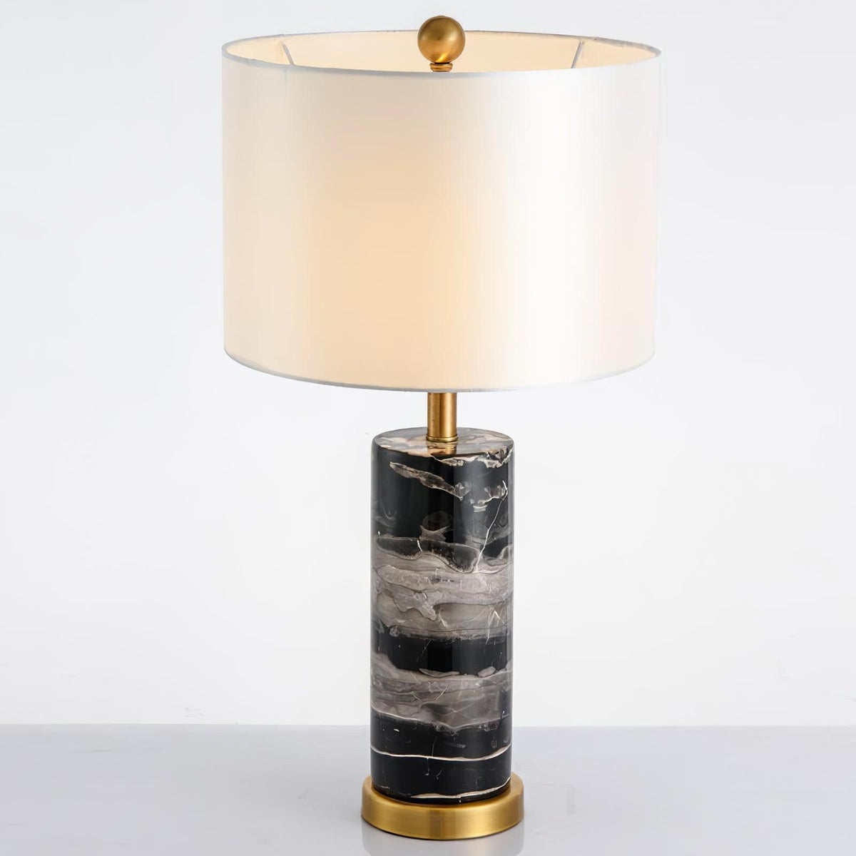 Close full-length shot of the Clérachic table lamp on white, its lit shade set above the black marble base.