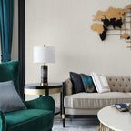 The Clérachic table lamp stands on a round side table beside a green velvet armchair and wall sculpture.