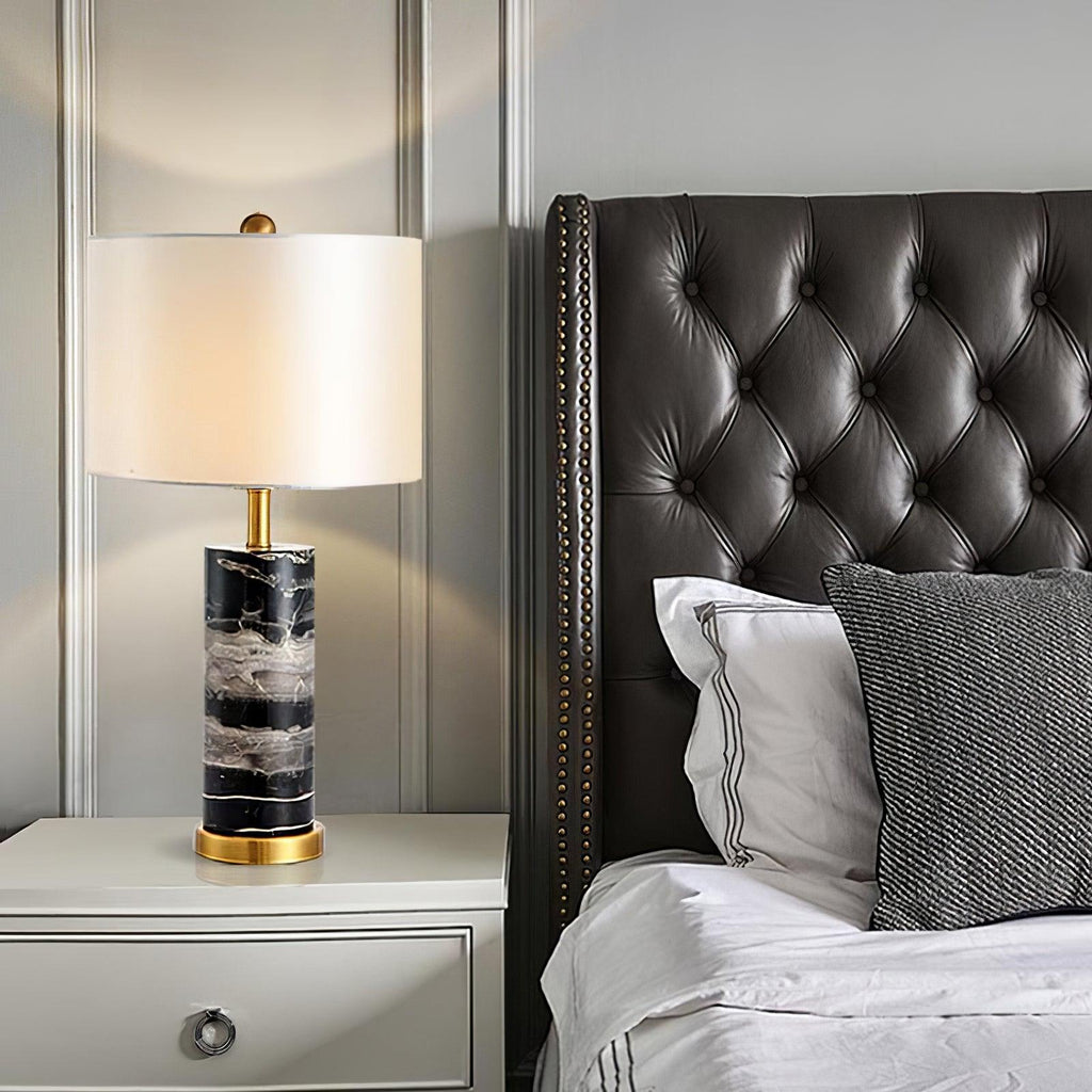 This Clérachic table lamp sits on a nightstand beside a tufted dark leather headboard and striped pillow.