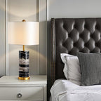 This Clérachic table lamp sits on a nightstand beside a tufted dark leather headboard and striped pillow.