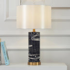 A Clérachic table lamp glows on a bedside surface with books stacked nearby against a white panelled wall.
