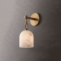 In brushed brass, this Clérachic wall light glows softly through its alabaster shade against a charcoal-grey wall.