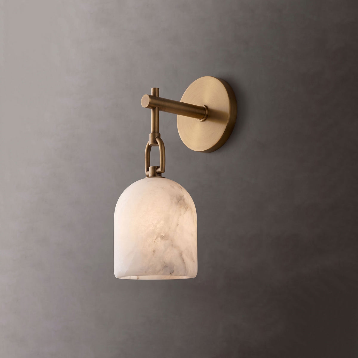 In brushed brass, this Clérachic wall light glows softly through its alabaster shade against a charcoal-grey wall.