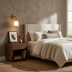 This brass Clérachic sconce lights a bedside wall above a walnut nightstand dressed with a framed print and dried flowers.