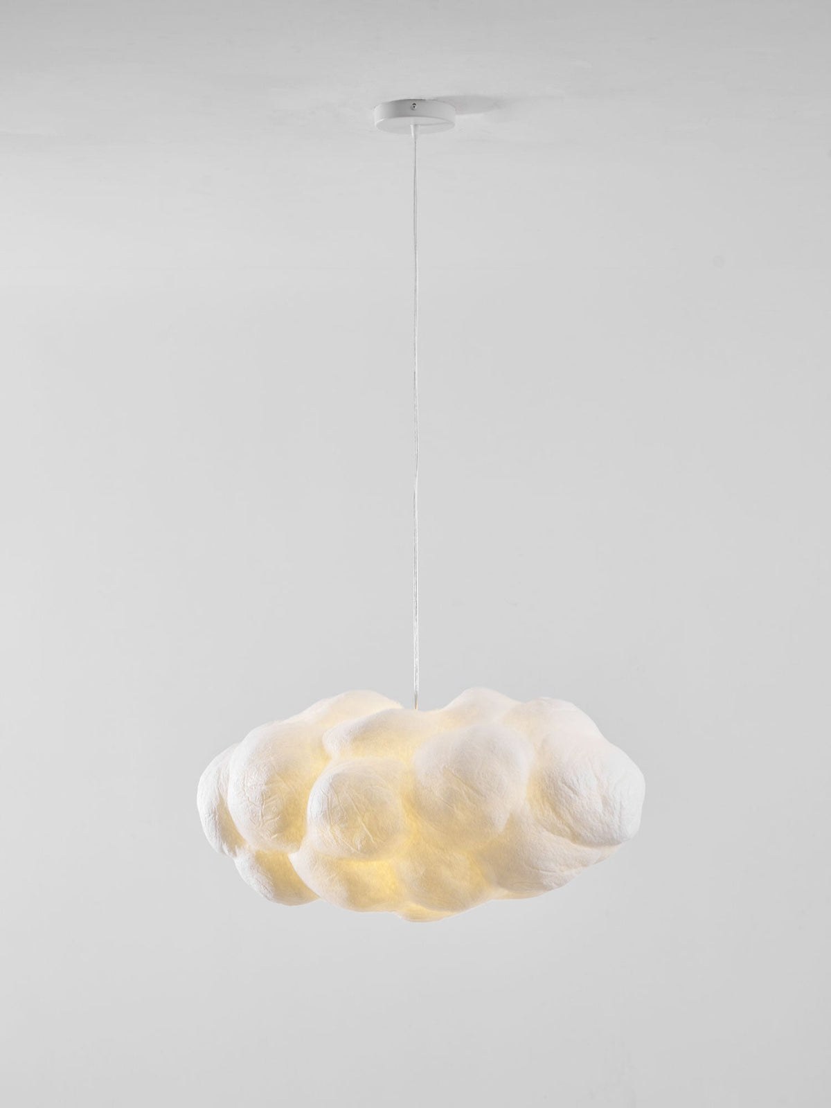 Lit warm against plain white, this Clérachic cloud-shaped pendant drapes from its ceiling mount.